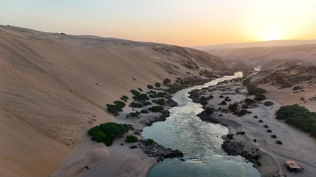 The Kunene River winding between the dunes at sunset
